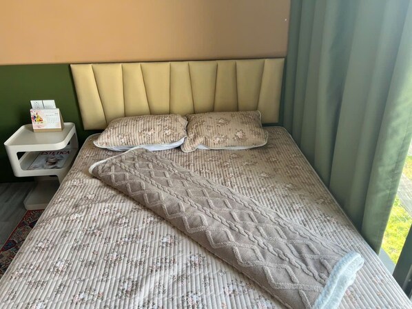 A bed with a patterned bedspread, two pillows, a nightstand with a calendar, and a green wall.