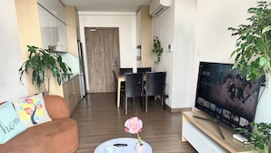 Un saló modern amb un sofà, una taula de centre amb una flor, una televisió i una zona de menjador al fons.