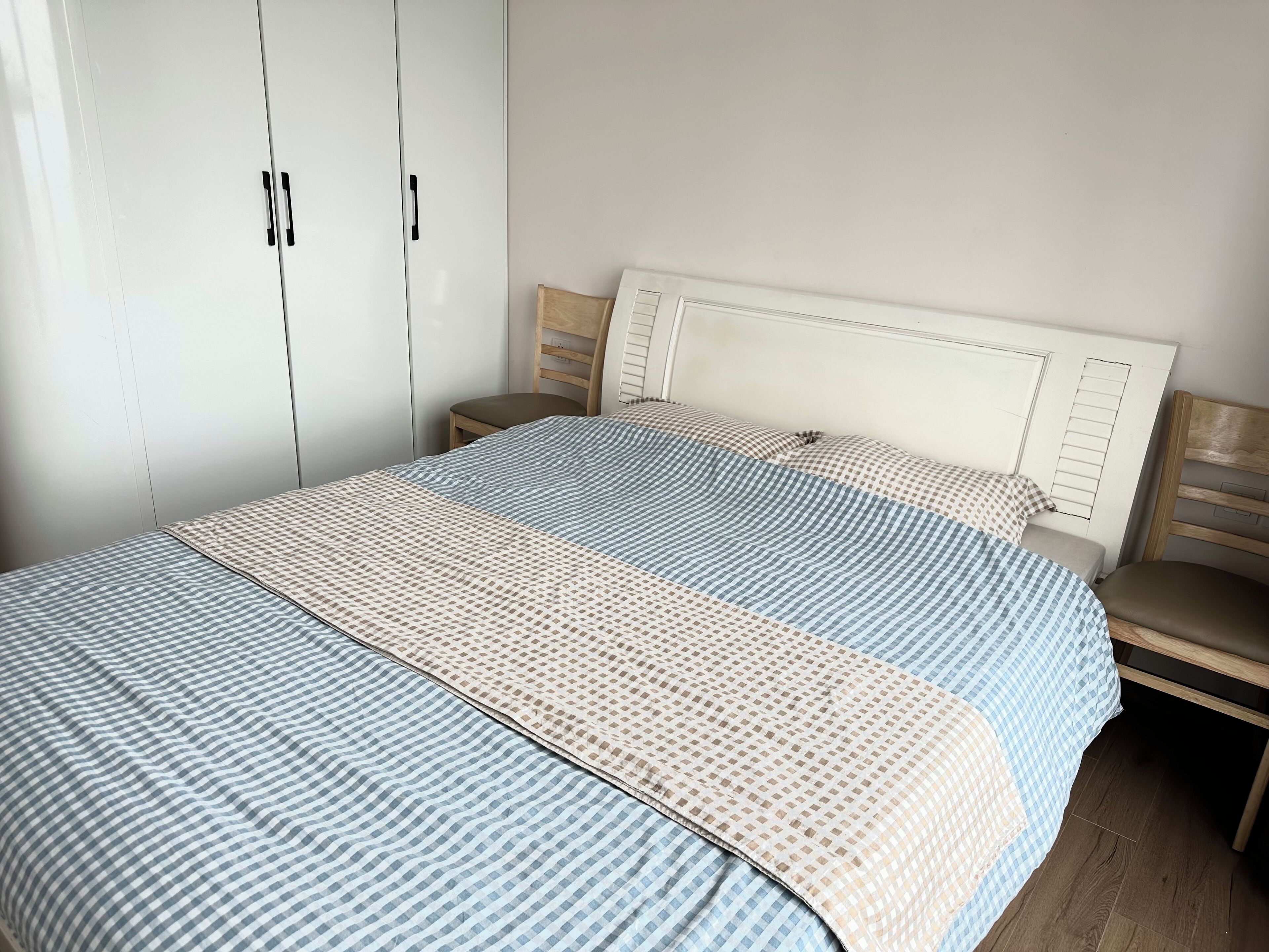 A bedroom with a bed, wooden headboard, nightstands, and a wardrobe.