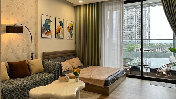 A modern bedroom with a bed, a sofa, a coffee table, and a view of a cityscape through large windows.