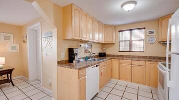 A compact kitchen with wooden cabinets, a dishwasher, a coffee maker, and a refrigerator.