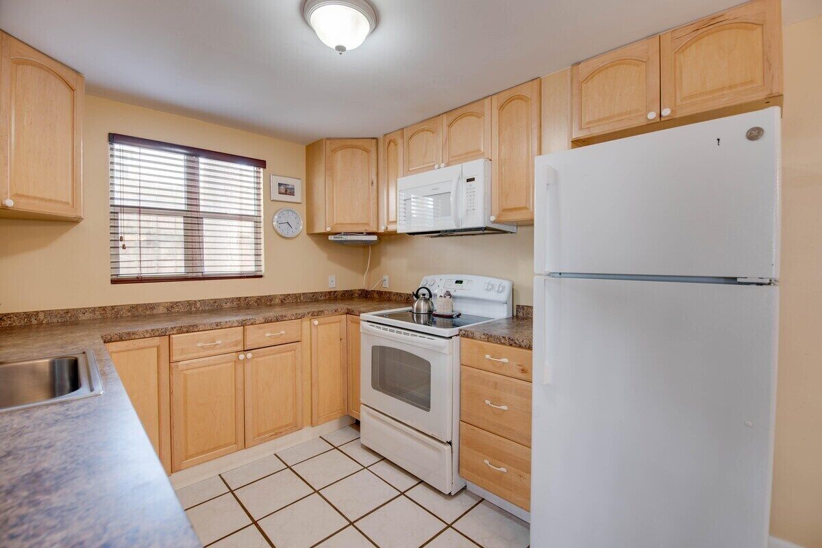 A kitchen with wooden cabinets, a white stove, a microwave, and a refrigerator.