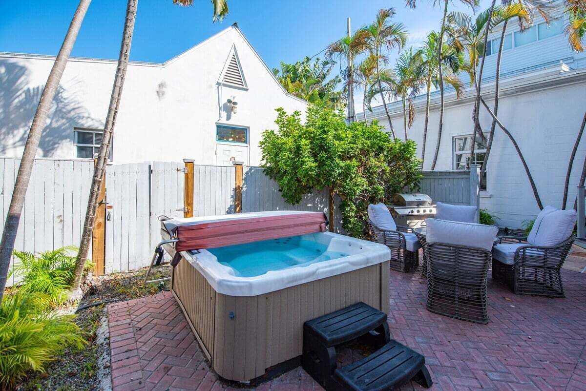 A backyard with a hot tub, wicker furniture, and a brick patio.