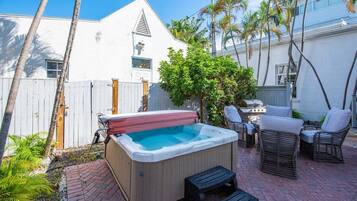 A backyard with a hot tub, wicker furniture, and a brick patio.