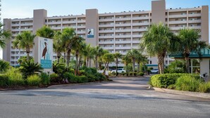 Un hôtel à plusieurs étages, doté d’une entrée centrale et entouré de palmiers et de verdure.