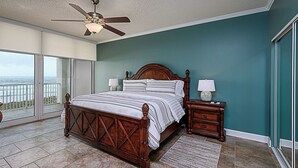 Une chambre dotée d’un grand lit, de deux tables de chevet, d’un ventilateur de plafond et offrant une vue sur l’océan grâce à de grandes portes coulissantes.