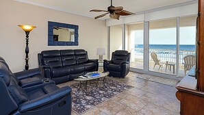 Un salon avec un canapé en cuir, des fauteuils, une table basse et une vue sur la plage grâce à de grandes portes vitrées.