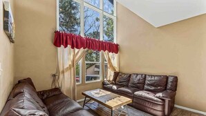A living room with two brown leather sofas, a wooden coffee table, and a large window with red valance. - Fanning Flagstaff (Flagstaff)