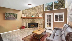 A living room with a brick fireplace, a leather sofa, and a large window. - Fanning Flagstaff (Flagstaff)