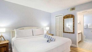 Une chambre à coucher avec un grand lit, des tables de chevet, un miroir et une porte donnant sur une salle de bain.