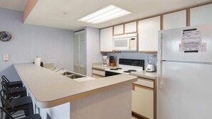 Une cuisine moderne dotée d’un îlot central, de meubles blancs, d’un four à micro-ondes, d’une cuisinière et d’un r éfrigérateur.