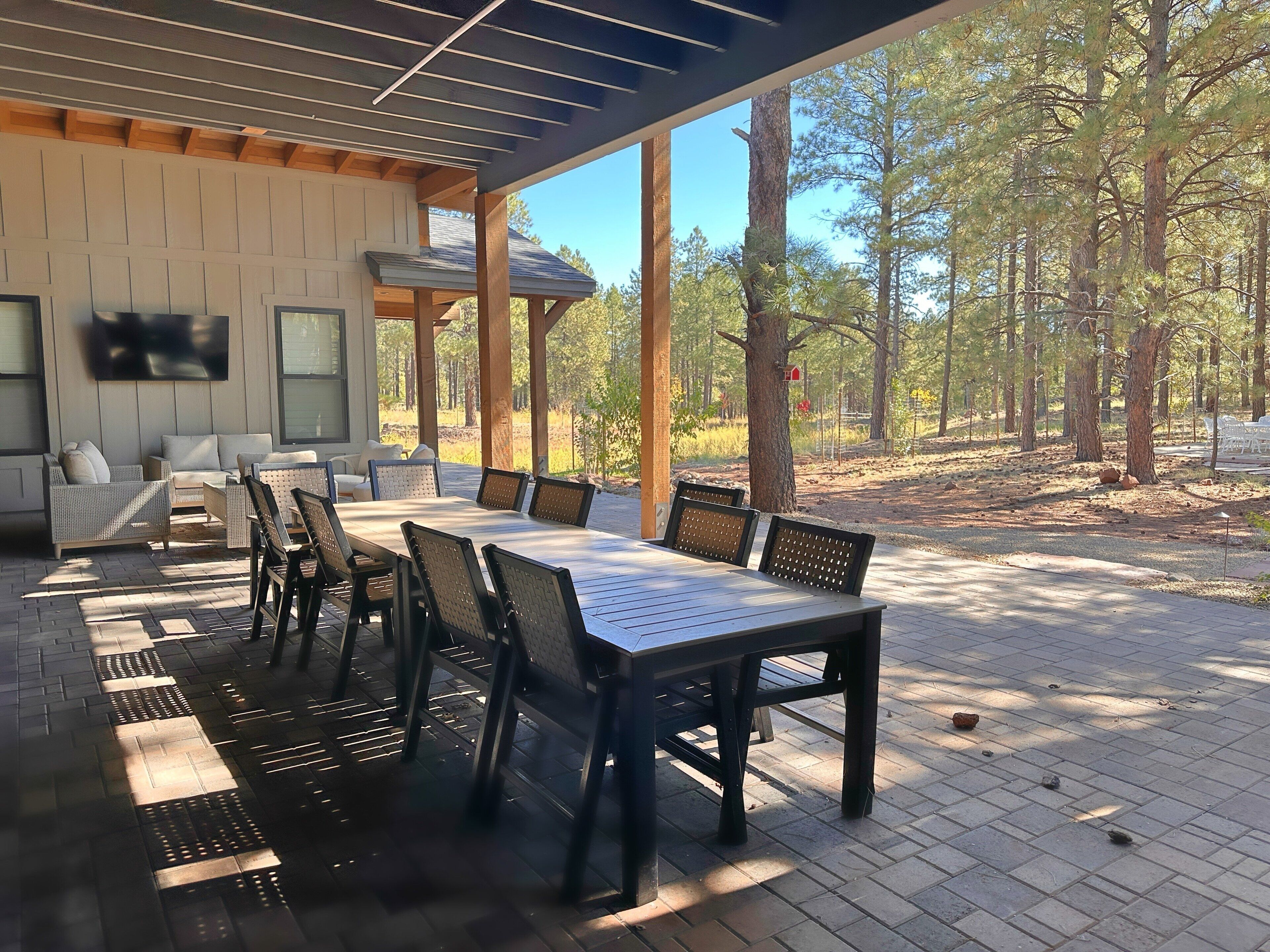An outdoor patio with a dining table and chairs, surrounded by wooden beams and a TV mounted on the wall.