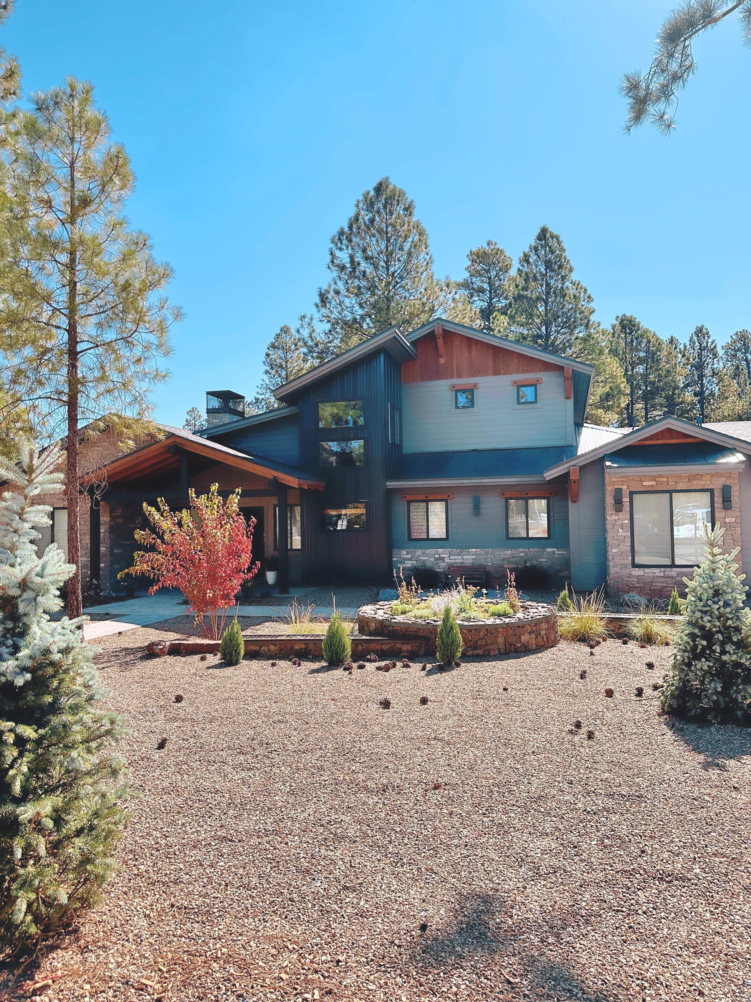 A modern two-story house with a stone foundation, a wooden deck, and a landscaped front yard with gravel and small shrubs.