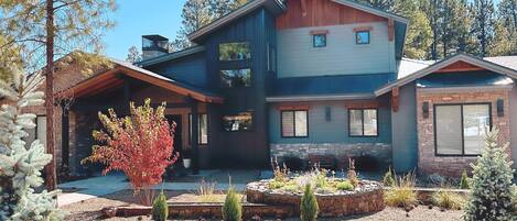 A modern two-story house with a stone foundation, a wooden deck, and a landscaped front yard with gravel and small shrubs.