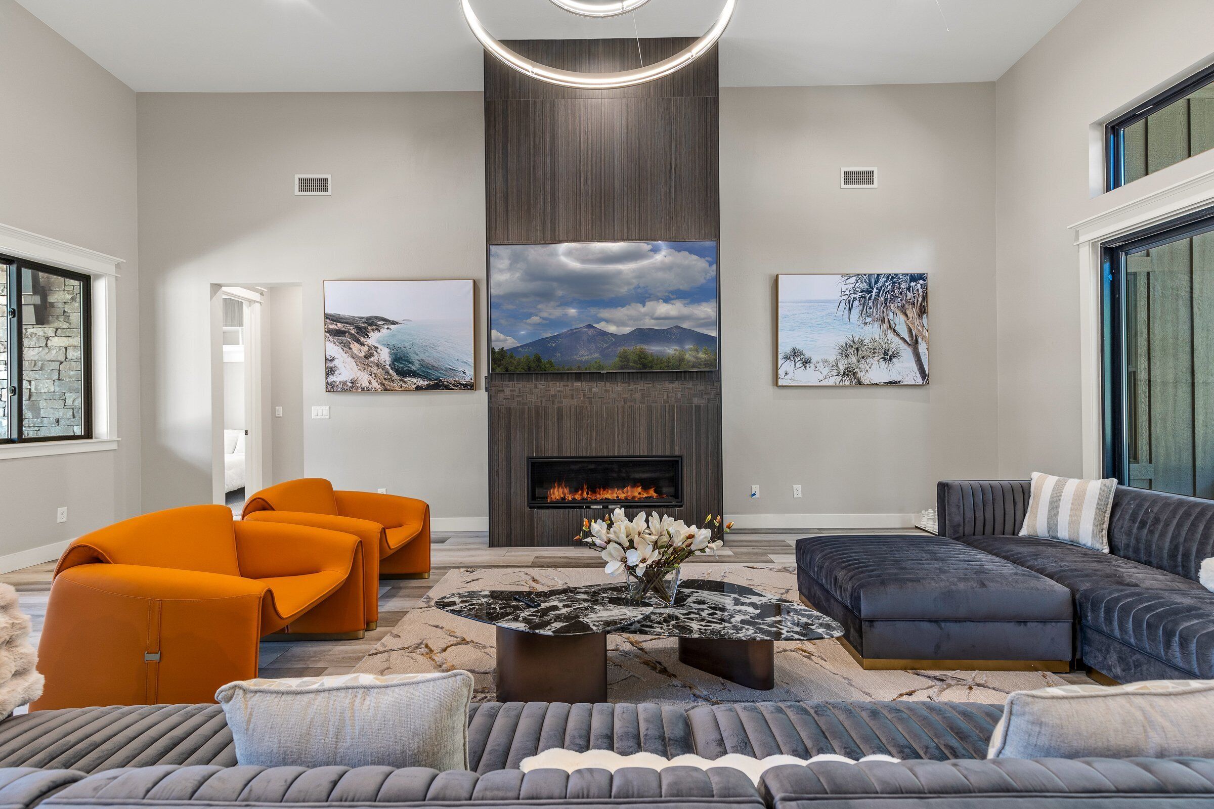 A modern living room with a fireplace, orange and gray sofas, and artwork on the walls.