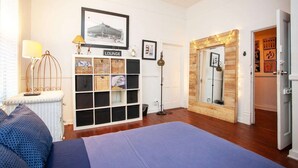 A room with a bed, a lounge area with baskets, a framed picture, a mirror, and a door with a sign. - Charming Ybor City Bungalow with Private Pool Oasis (Tampa)