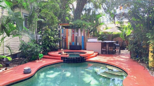 A swimming pool with a red deck, surrounded by lush greenery and a small outdoor seating area. - Charming Ybor City Bungalow with Private Pool Oasis (Tampa)