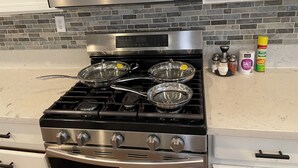 A kitchen with a gas stove, a microwave above it, and various cooking utensils and seasonings on the counter.