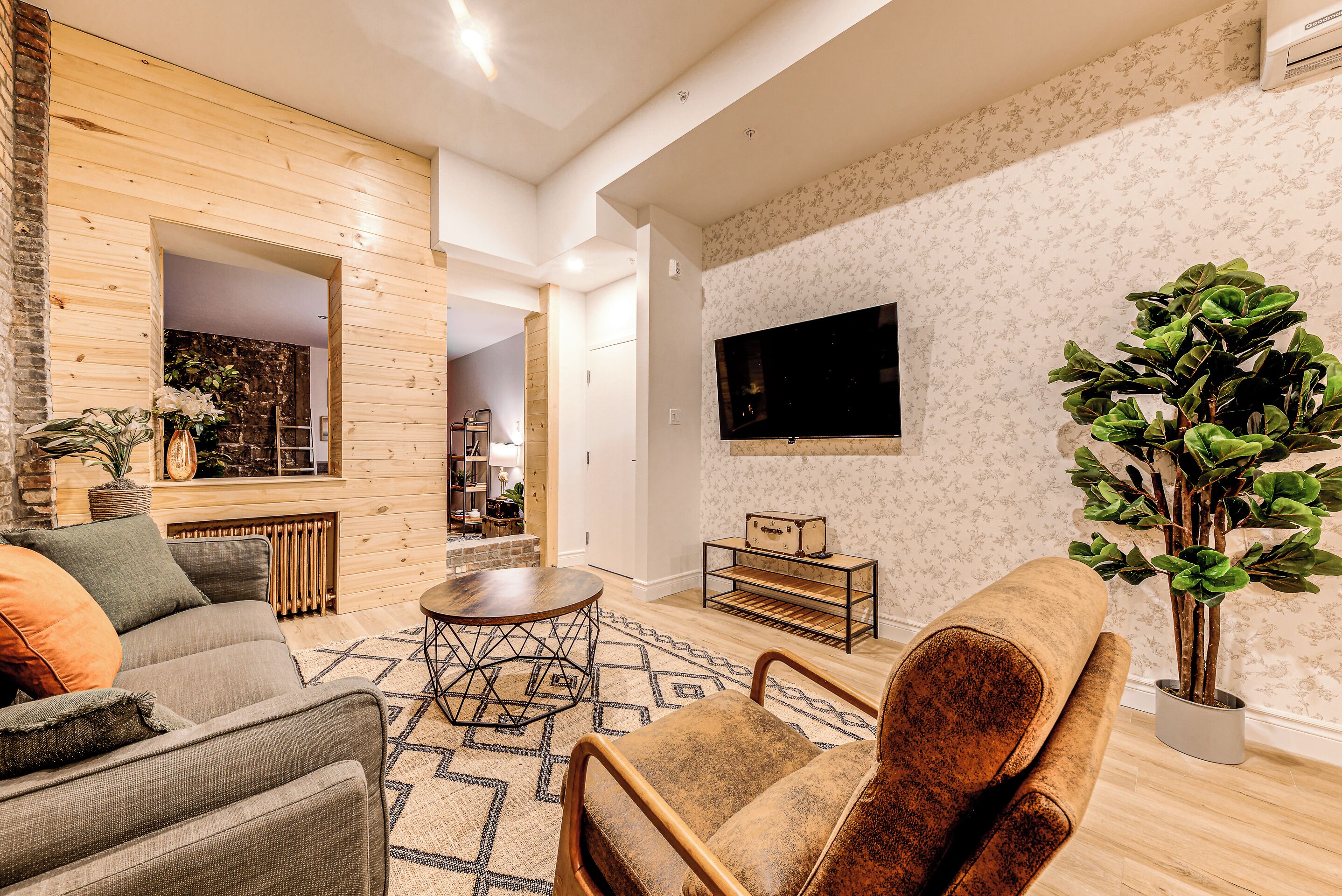 Un salon moderne avec un canapé, des fauteuils, une table basse et un téléviseur fixé au mur.