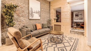 A cozy living room with a brick wall, a wooden floor, a grey sofa, a wooden coffee table, and a patterned rug. - Bohemian Vieux Quebec Two Bedroom (Québec City)