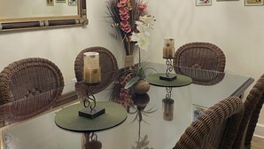 Un coin repas avec une table en verre, des chaises en osier, un lustre et des tableaux accrochés au mur.