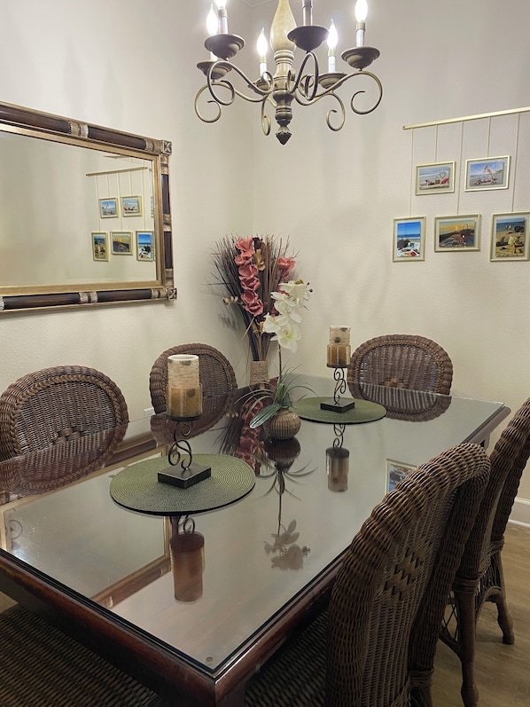 A dining area with a glass table, wicker chairs, a chandelier, and wall-mounted pictures.