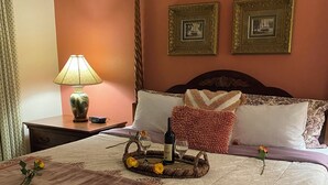 Un lit bien fait, recouvert d’une couvre-lit à motifs, une table de chevet avec une lampe, et deux tableaux encadrés accrochés au mur.