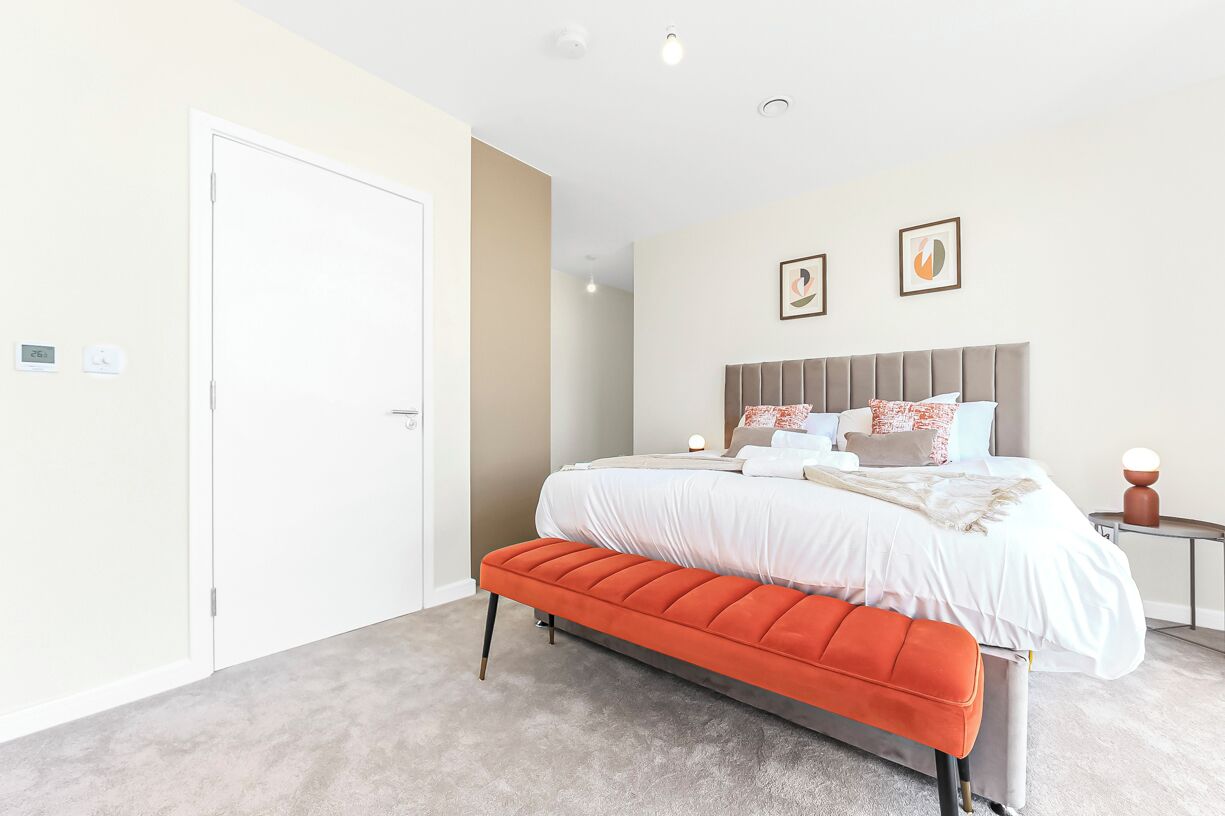 A modern bedroom with a large bed, a bench, a bedside table, and two framed pictures on the wall.