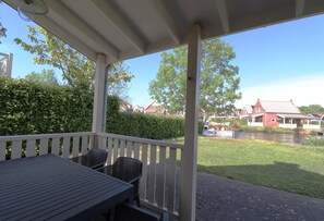 A covered outdoor area with a table and chairs, overlooking a canal with houses and greenery. - Bungalow by Water Near Rotterdam (Simonshaven)