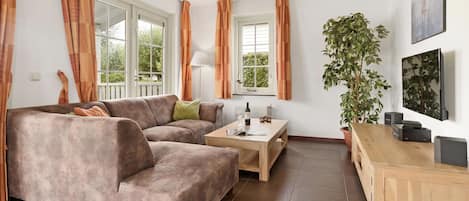 A living room with a brown sofa, a coffee table, a TV, and a plant.