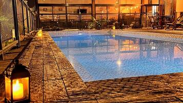 A nighttime swimming pool with a wooden deck, a lantern, and a building in the background.