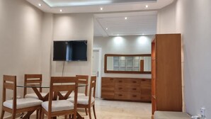 A room with a dining table and chairs, a TV mounted on the wall, a wooden cabinet, and a mirror.