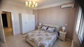 A bedroom with a bed, bedside tables, a wardrobe, a chandelier, and an air conditioning unit.