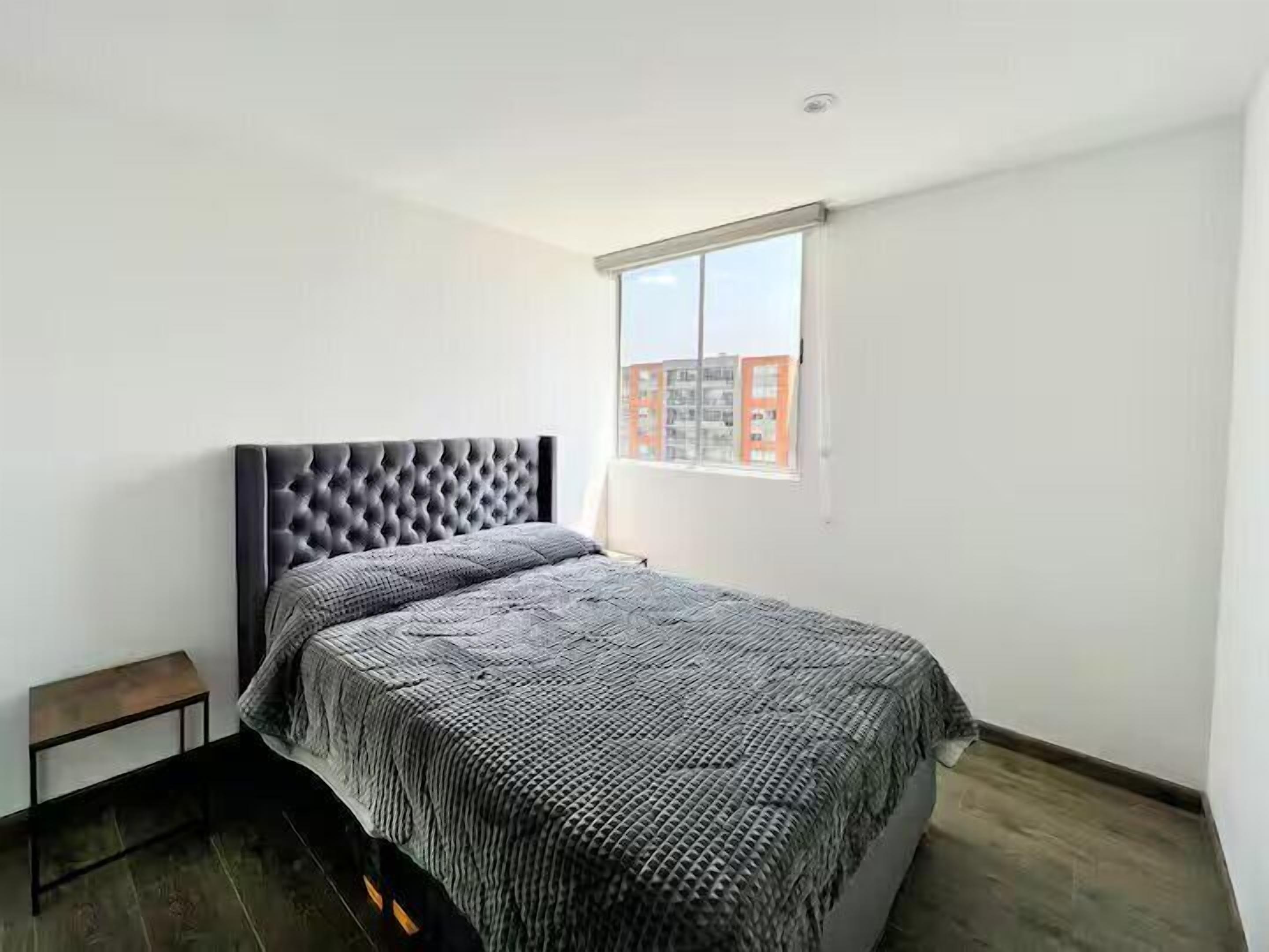 Un dormitorio con una cama grande, un banco pequeño y una ventana con vista a la ciudad.