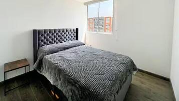 Un dormitorio con una cama grande, un banco pequeño y una ventana con vista a la ciudad.