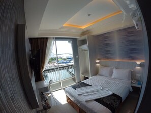 Una camera d'albergo con un letto, un comodino, una finestra con tende e vista sulla città.