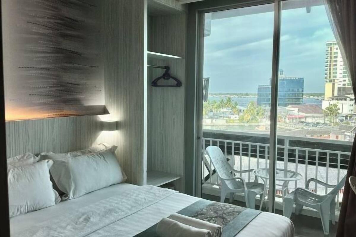 A hotel room with a large bed, a view of the city, and a balcony with chairs.