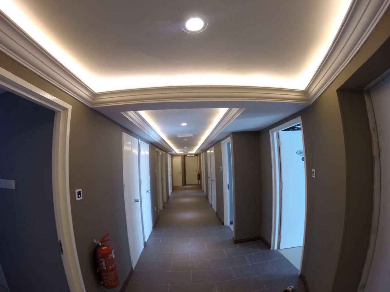 Corridoio d'albergo con porte su entrambi i lati, un estintore e un soffitto con illuminazione a incasso.