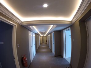 Corridoio d'albergo con porte su entrambi i lati, un estintore e un soffitto con illuminazione a incasso.