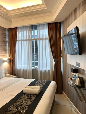 Una camera d'albergo con un letto, una televisione, un comodino, una finestra con tende e vista all'esterno.
