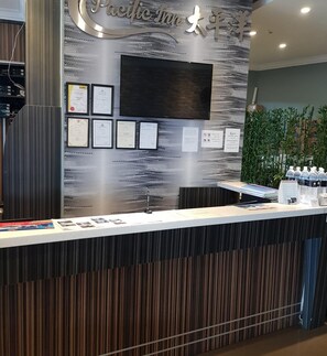 A reception desk with a modern design, featuring a digital screen, framed certificates, and a menu board. - Pacific Inn (Semporna)