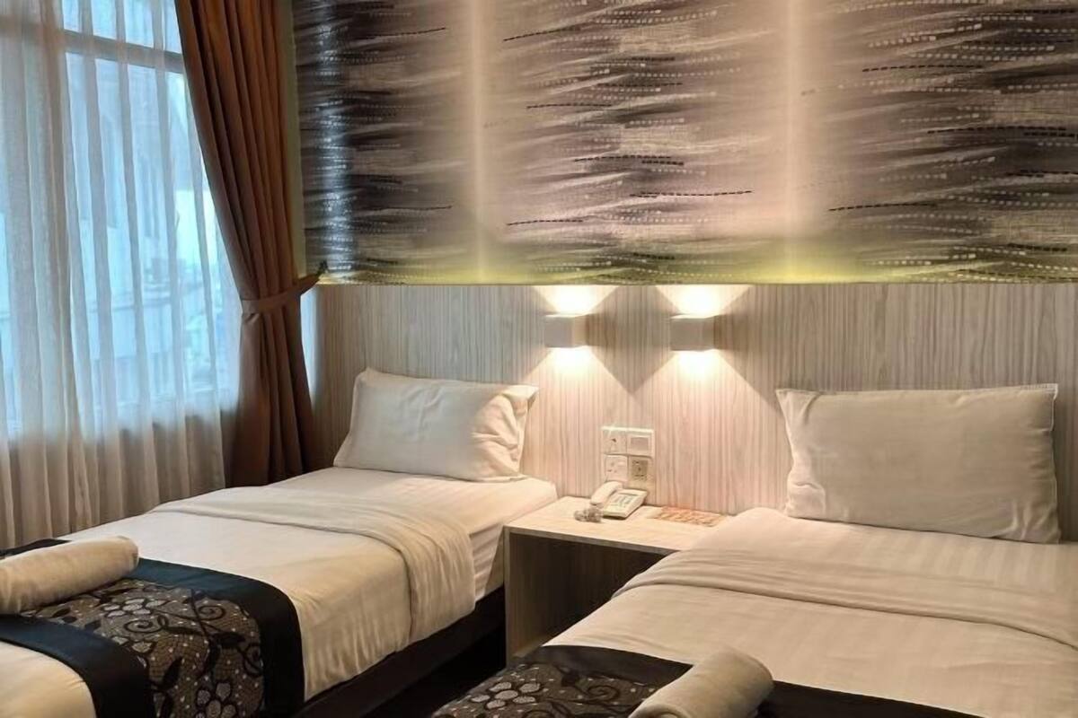 A hotel room with two beds, a nightstand with a phone, and a window with curtains.