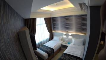 Camera d'albergo con due letti, un'ampia finestra con tende, un condizionatore d'aria a muro e una lampada a soffitto.