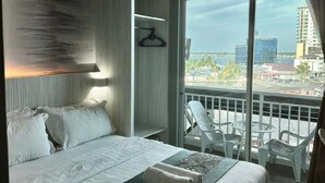 Une chambre d’hôtel avec un grand lit, une vue sur la ville et un balcon équipé de chaises.