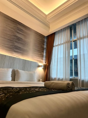 A hotel room with a large bed, a headboard with a textured design, a window with sheer curtains, and a wall-mounted light fixture. - Pacific Inn (Semporna)