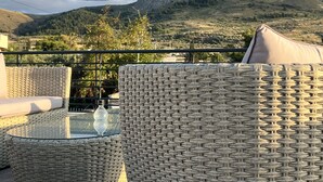 A wicker outdoor seating area with a glass table, overlooking a mountainous landscape. - Apollonio Suites (Corinth)