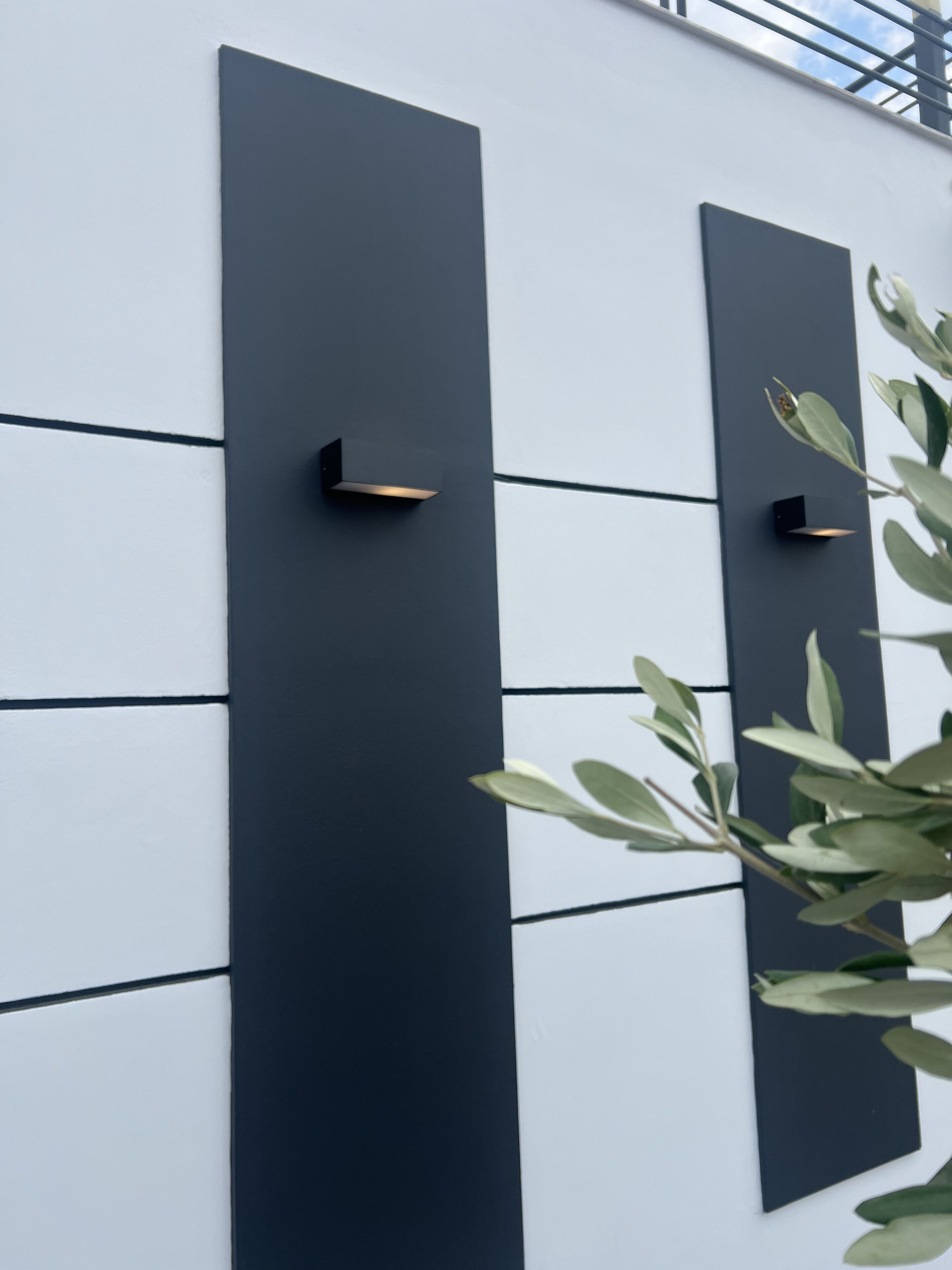Fachada de edificio moderno con paneles horizontales y dos paneles verticales negros con luminarias integradas.