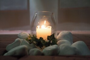 A candle in a glass holder surrounded by stones on a wooden surface. - Apollonio Suites (Corinth)