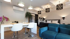 A modern living space with a kitchen area, a dining table with bar stools, a blue sofa, and pendant lighting. - Apollonio Suites (Corinth)