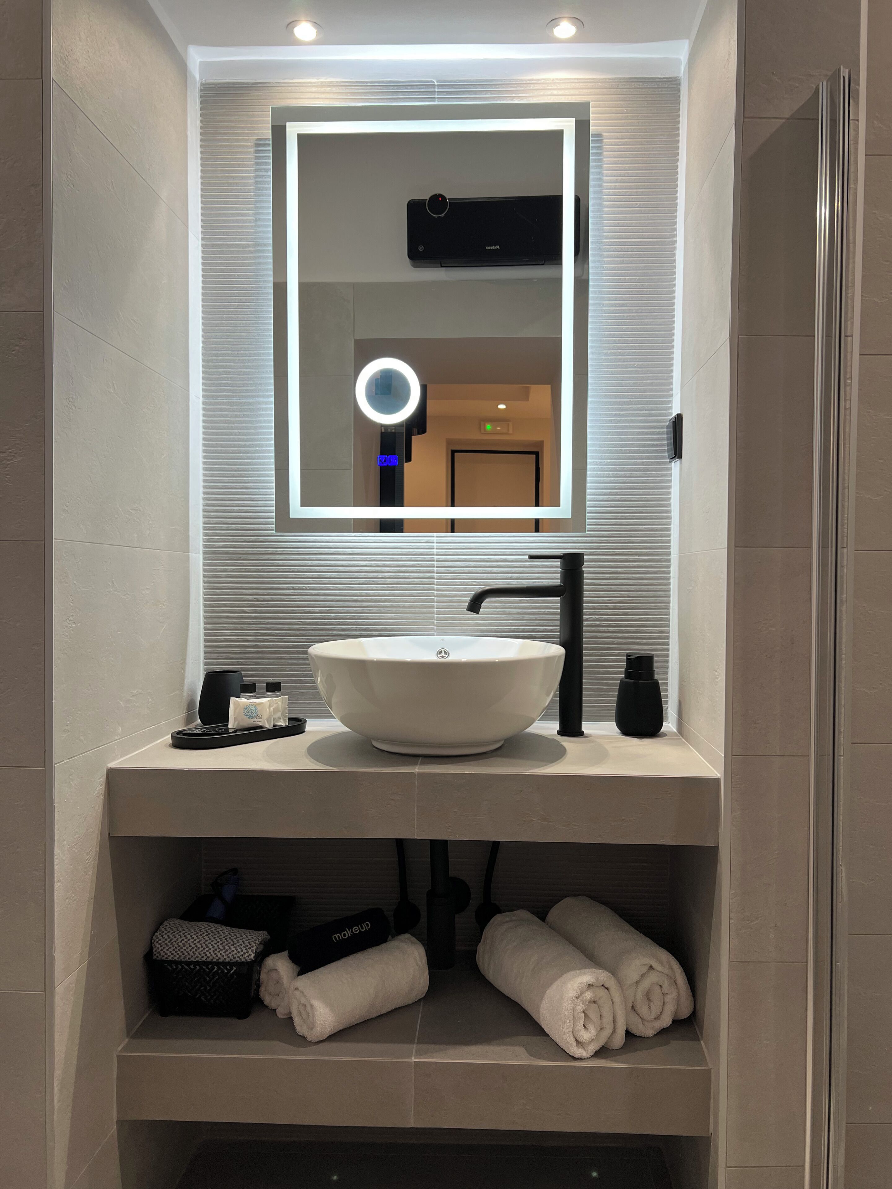 A modern bathroom with a large mirror, a round vanity mirror, a white sink, and a towel rack.